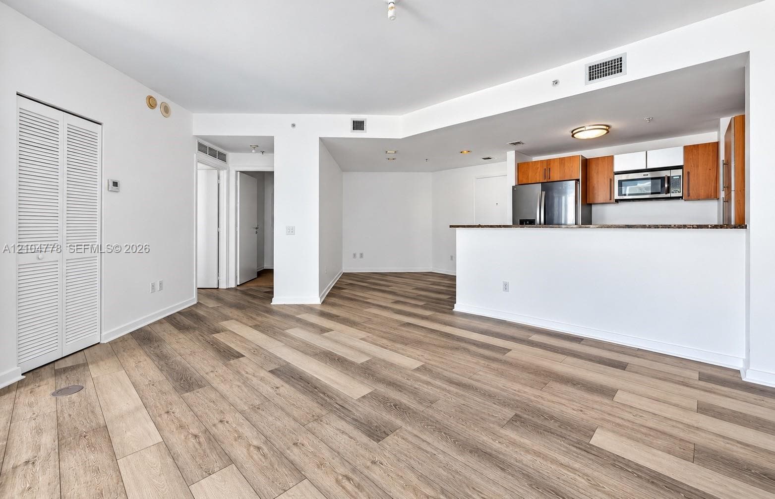 Wood-finish flooring throughout, kitchen with wood cabinetry, stainless steel appliances, and a built-in microwave, white louvered closet doors, and recessed lighting