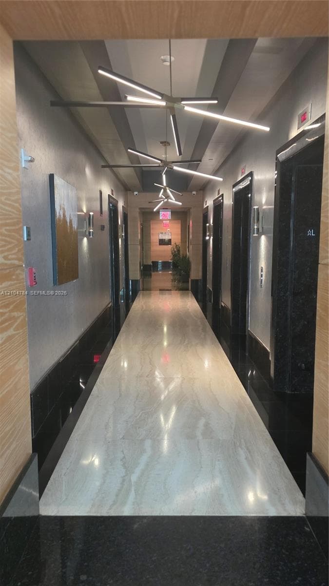 Hallway featuring polished stone flooring, dark stone wall accents, linear LED pendant lighting, and wood-finish wall paneling
