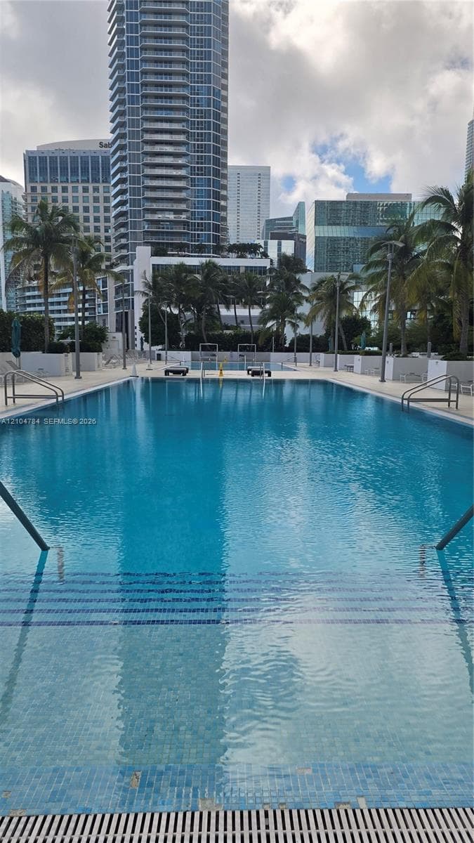In-ground lap pool featuring a tiled finish, submerged entry steps, stainless steel handrails, and surrounding hardscaping
