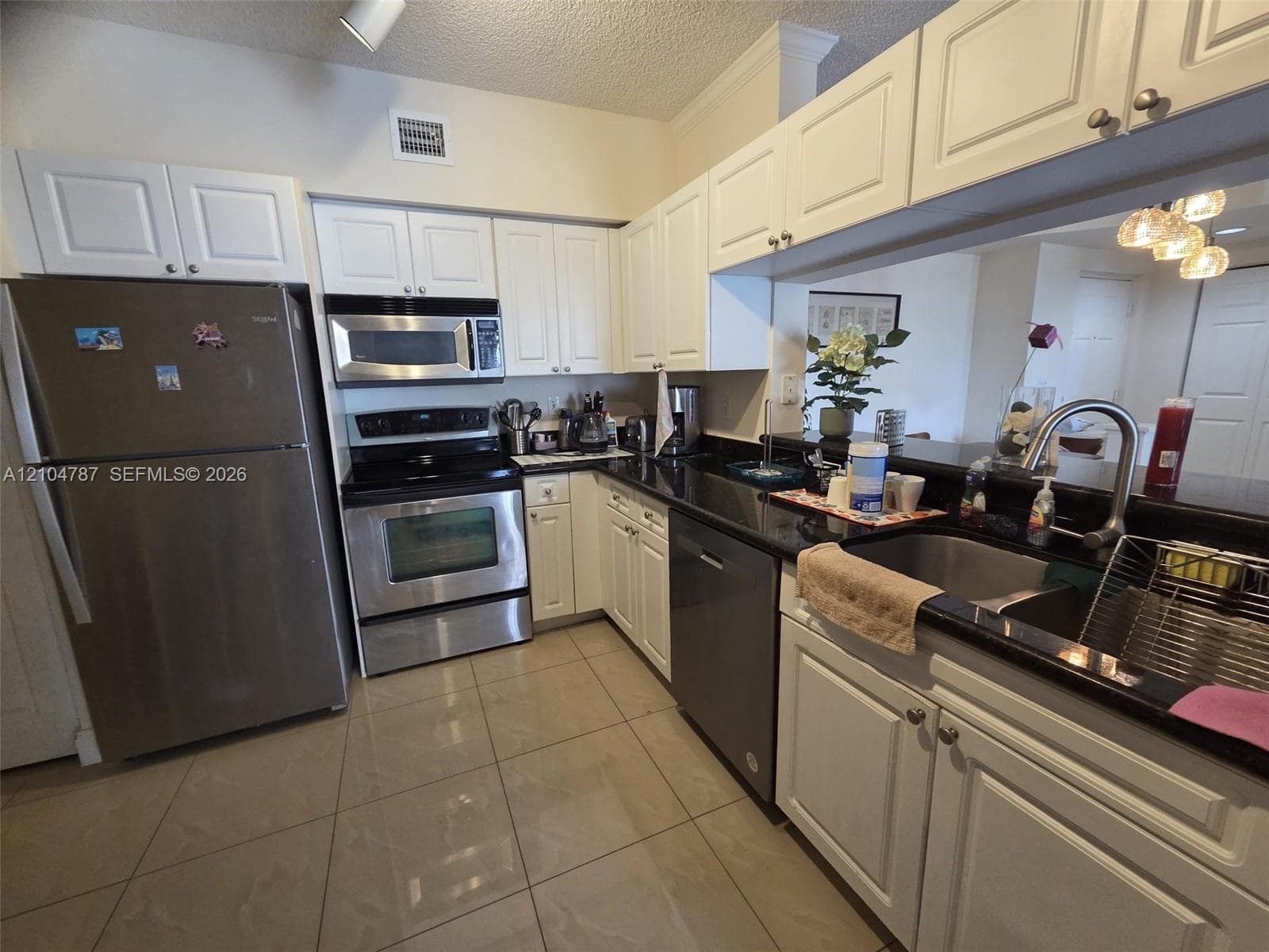 Kitchen featuring white raised-panel cabinetry, black stone countertops, stainless steel appliances, and large-format tile flooring