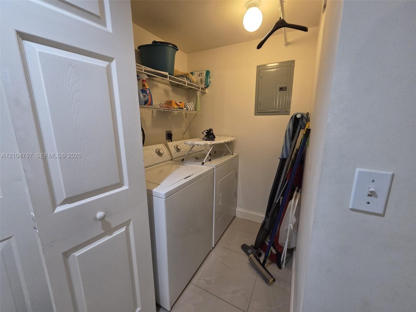 Laundry closet featuring white panel door, large-format tile flooring, and overhead wire shelving