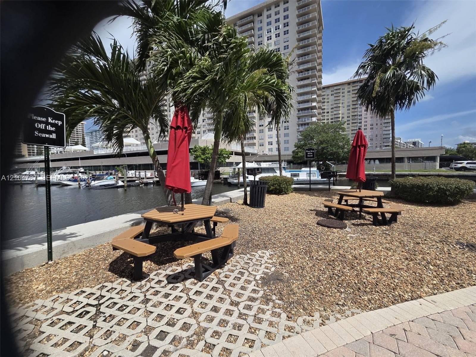 Waterfront grounds featuring a seawall, gravel landscaping, mature palm trees, and integrated concrete pavers