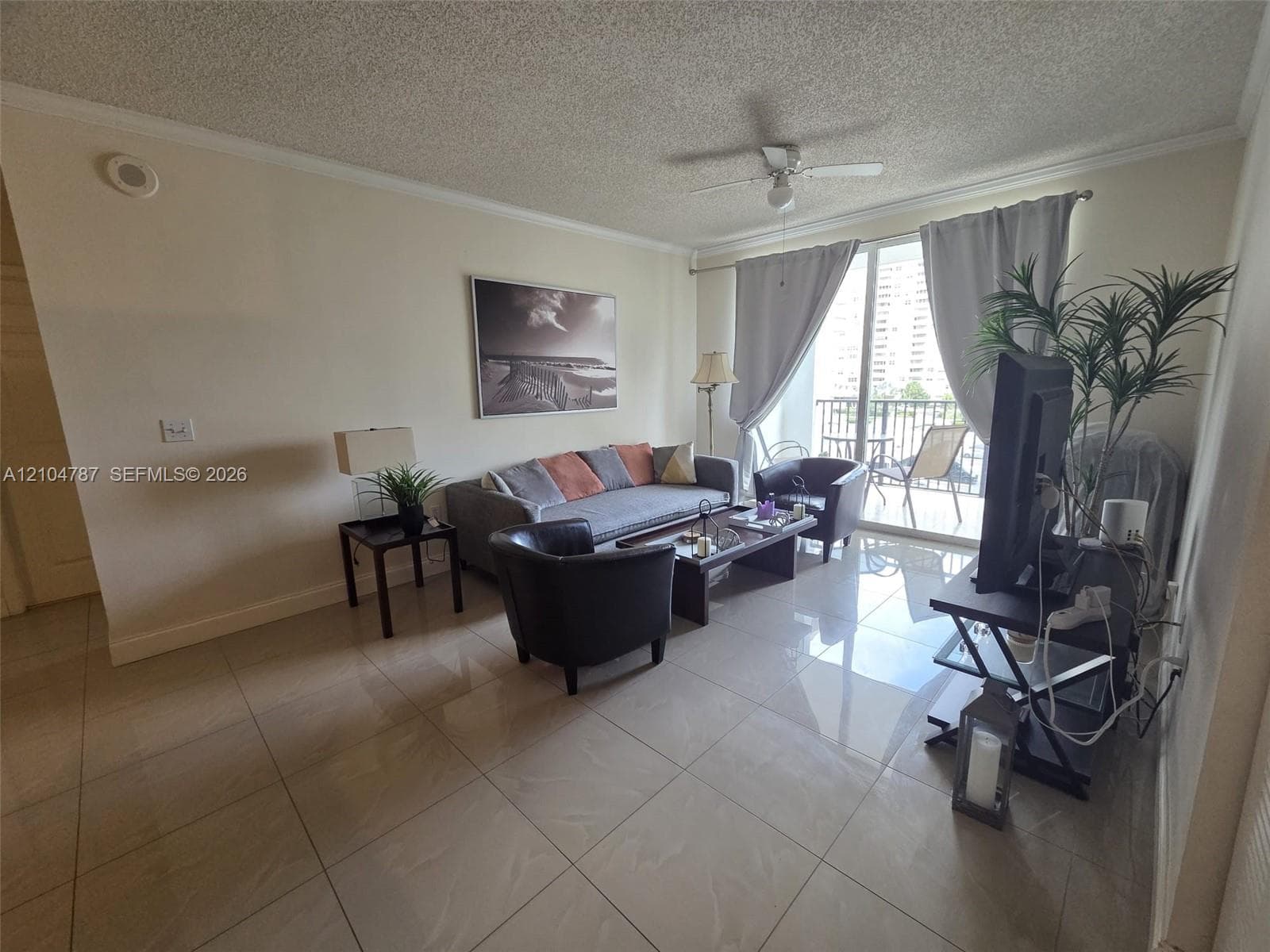 Living area featuring large-format tile flooring, ceiling fan, and sliding glass doors providing outdoor access