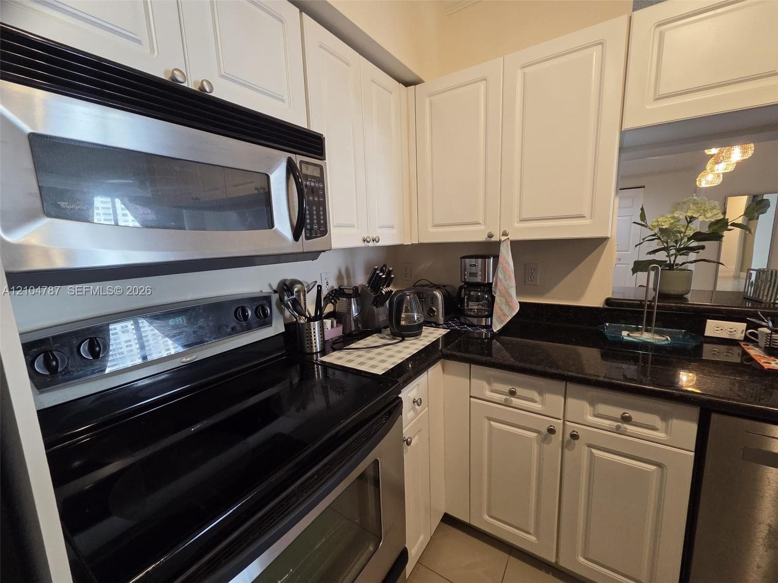 White cabinetry with silver-tone hardware, dark solid-surface countertops, built-in stainless steel microwave, and integrated electric range