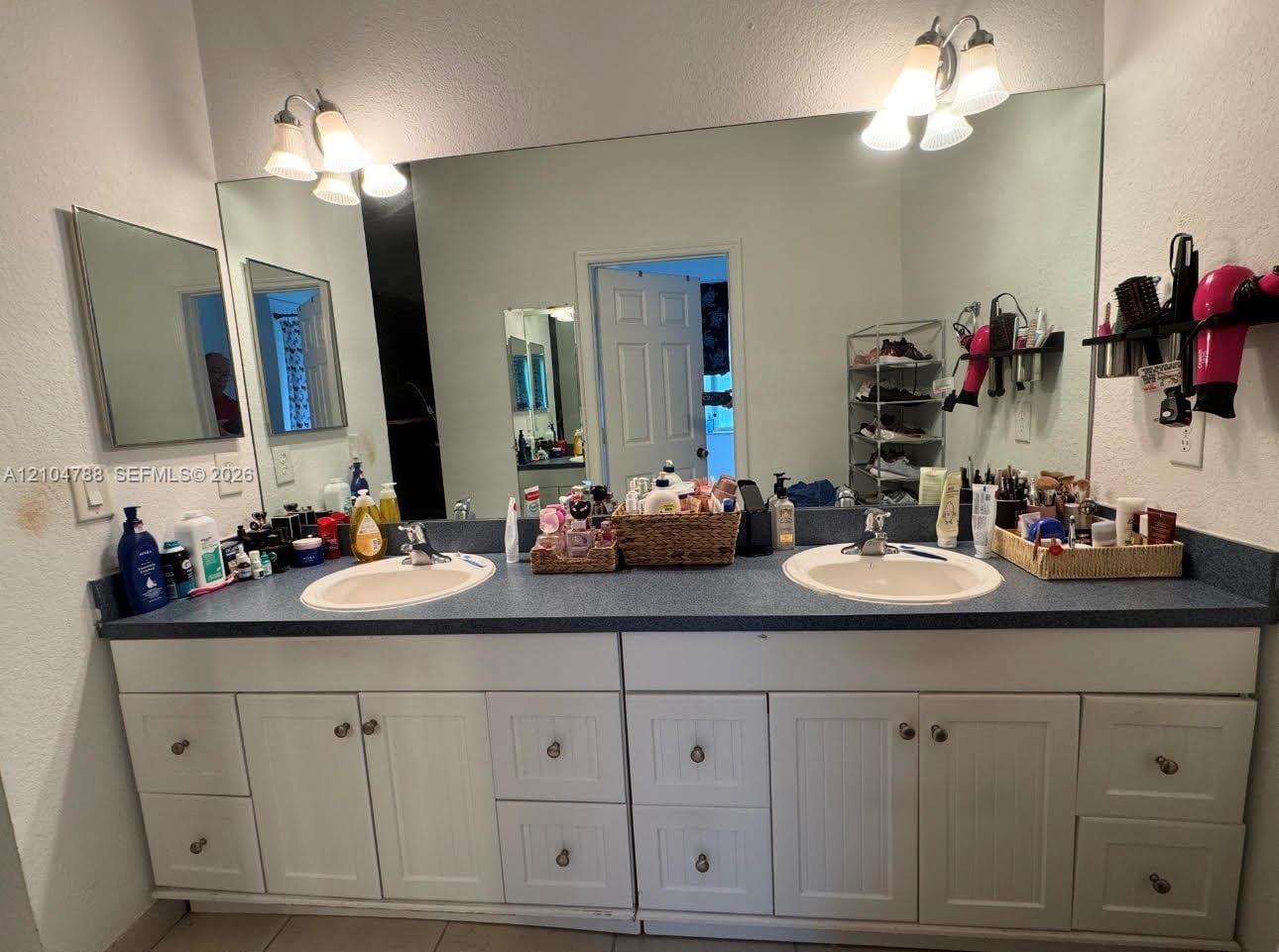 Double vanity featuring white beadboard-style cabinetry, solid-surface countertops with integrated dual sinks, and two tri-light vanity fixtures