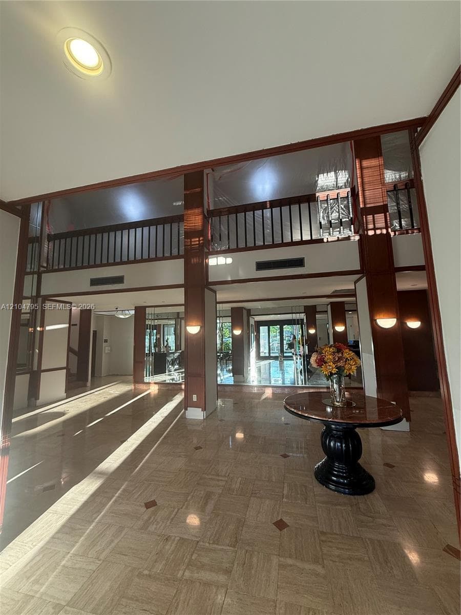 Grand foyer featuring high ceilings, polished stone tile flooring with decorative inlay, wood-trimmed columns, and a mezzanine with a dark wood railing