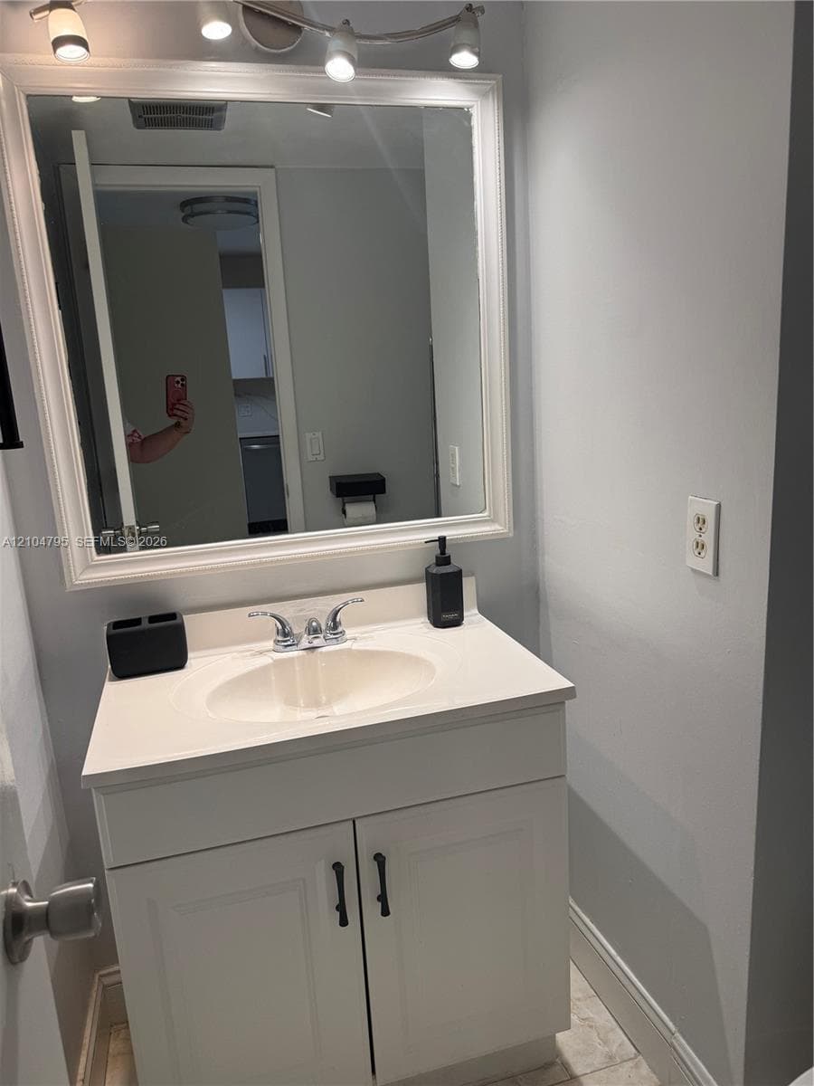 White vanity with a solid surface countertop, integrated oval sink, chrome dual-handle faucet, framed wall mirror, and multi-bulb overhead light fixture