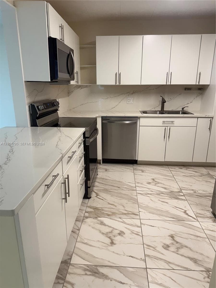 Kitchen featuring white shaker-style cabinetry, white countertops with grey veining, stone-finish floor tiling, and stainless steel appliances