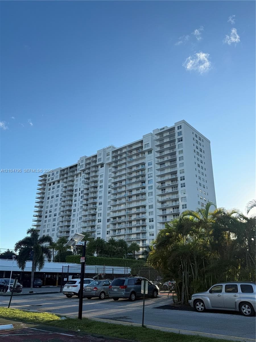 High-rise residential exterior featuring white facade, multi-story balconies, and mature palm trees