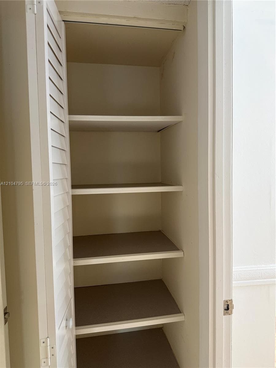 Built-in storage cabinet featuring louvered door panels and four fixed interior shelves