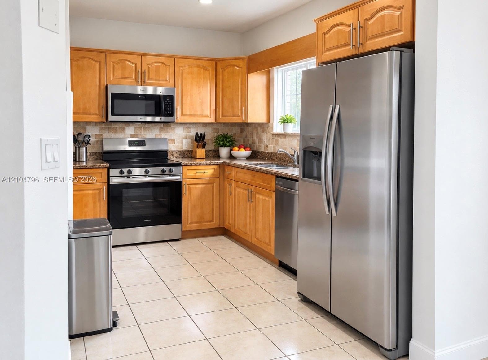 Kitchen featuring natural wood cabinetry, stone-finish countertops, tile backsplash, tile flooring, and stainless steel appliances