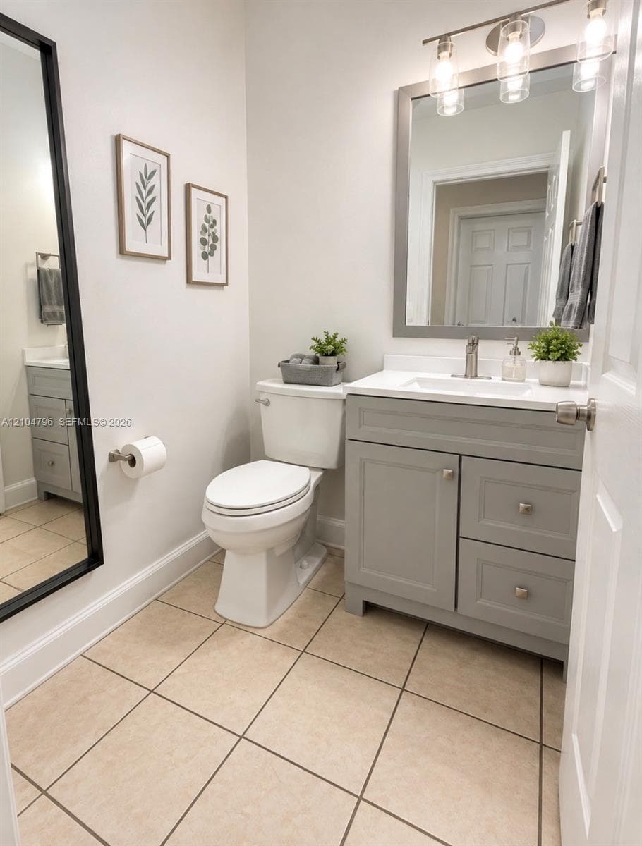 Bathroom featuring a grey vanity with satin-finish hardware, a crisp white countertop with an integrated sink, ceramic tile flooring, and a framed mirror with three-light fixture