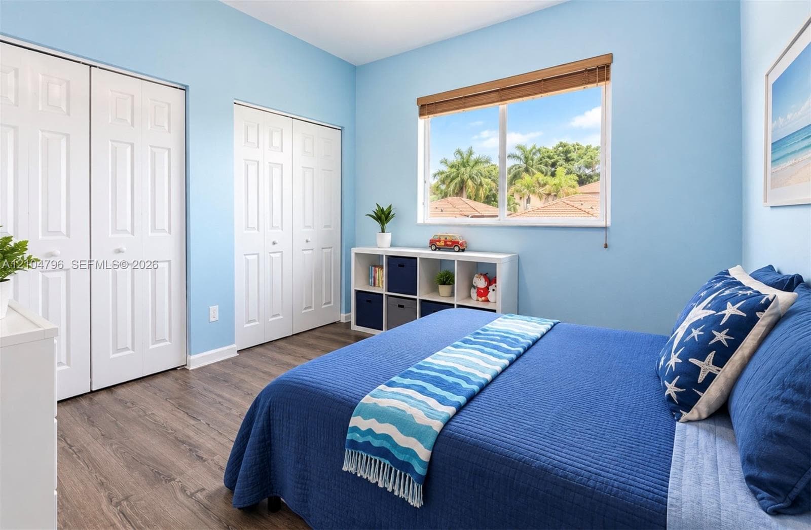 Room featuring wood-finish flooring, dual-door closets, and a window with wood-slat blinds