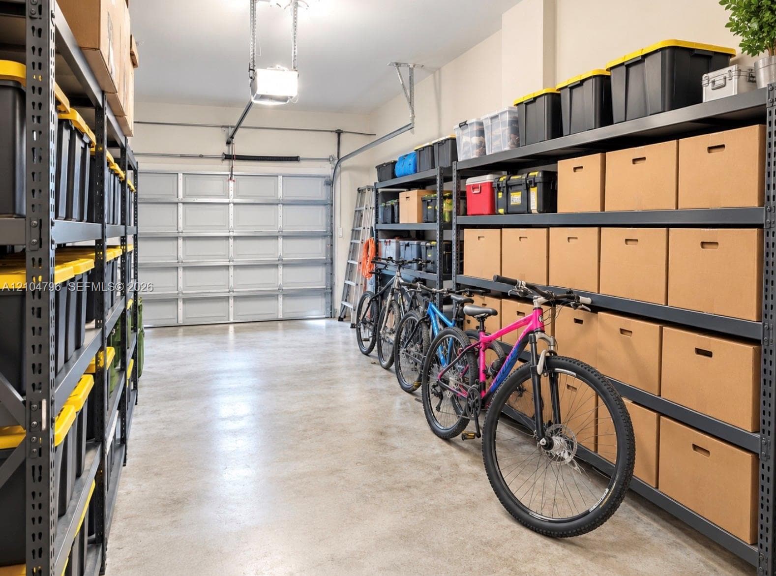 Garage space featuring finished concrete flooring, a sectional overhead garage door, and extensive industrial-style metal storage shelving