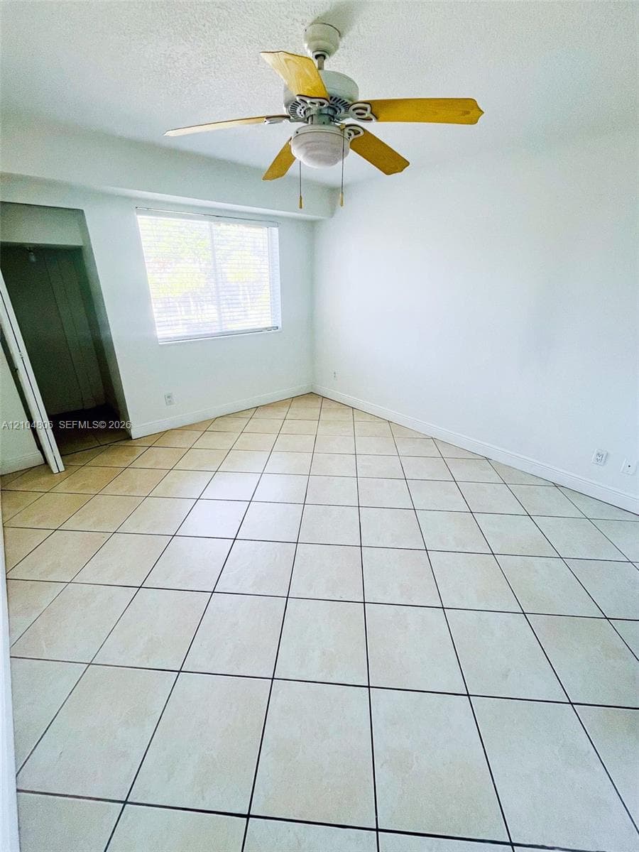 Room featuring tile flooring, white walls, a window with blinds, and a ceiling fan with light fixture
