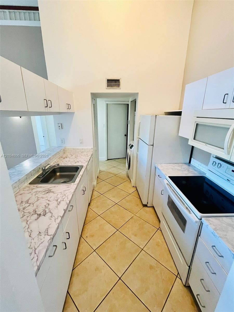 Kitchen featuring white cabinetry, a stainless steel sink, patterned countertops, and tile flooring