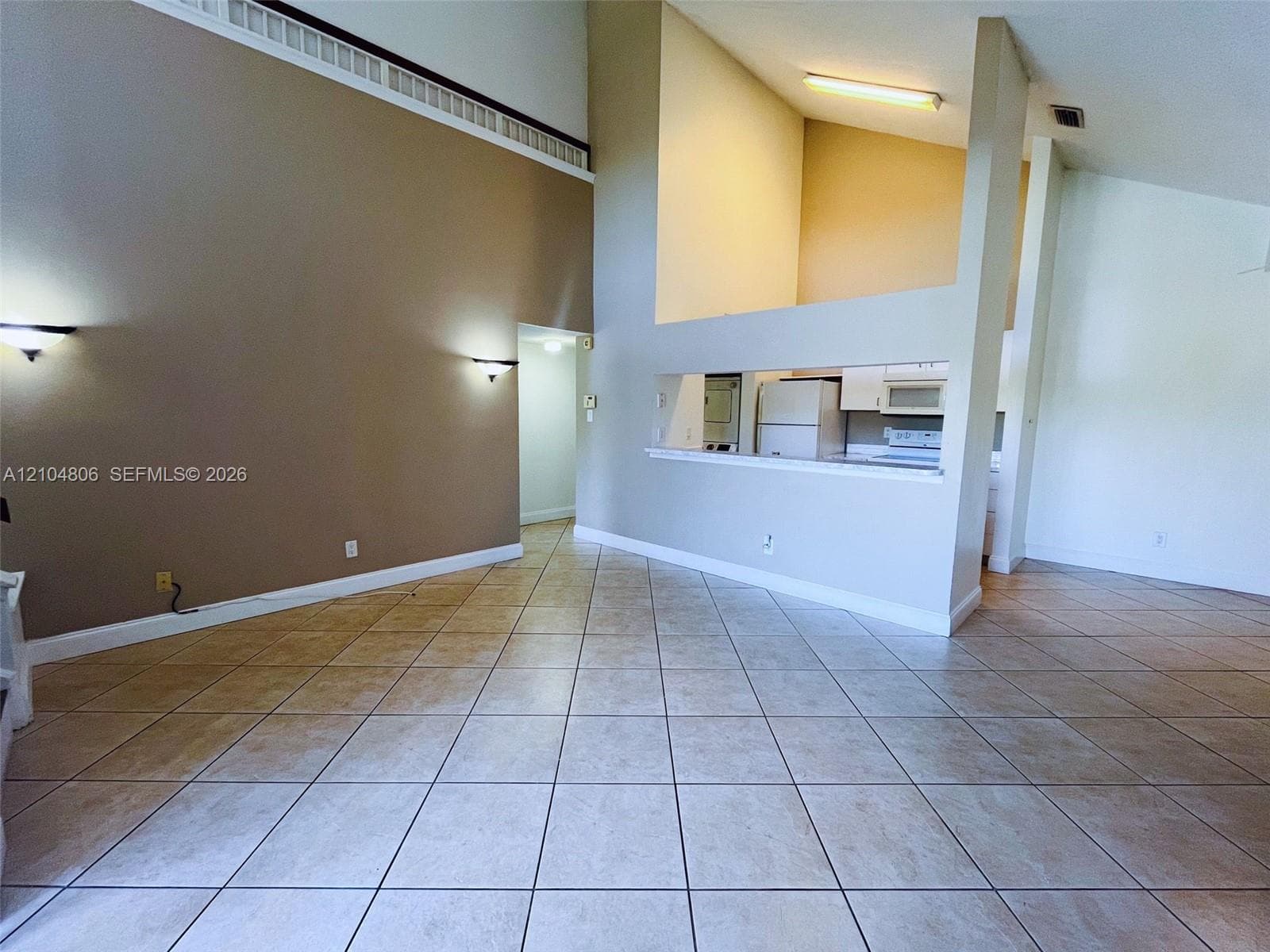 Vaulted ceilings, tiled flooring, built-in sconce lighting, and a partial wall opening to the kitchen area