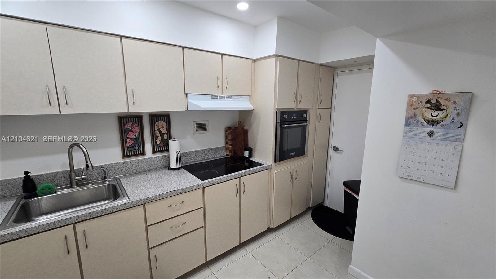 Kitchen featuring extensive light-toned cabinetry, built-in oven, integrated electric cooktop, stainless steel sink with a high-arc faucet, and light-colored countertops