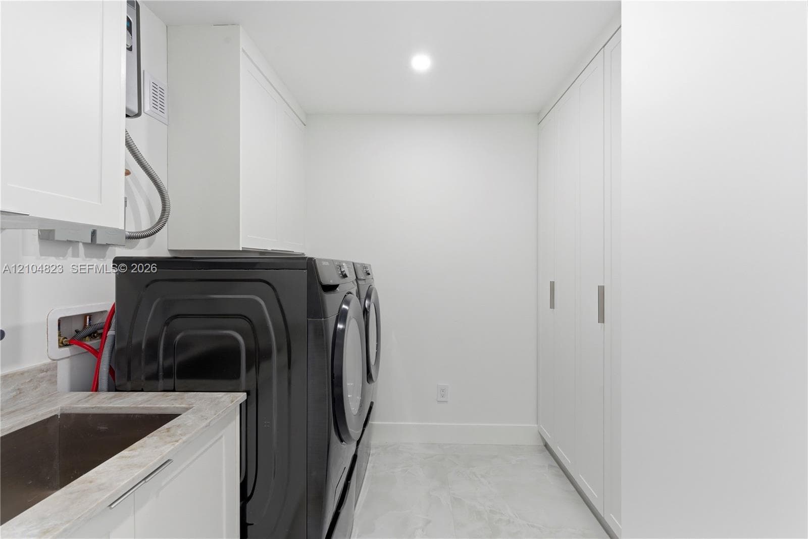 Integrated laundry area featuring full-height white cabinetry, a utility sink with a stone-finish countertop, and recessed ceiling lighting