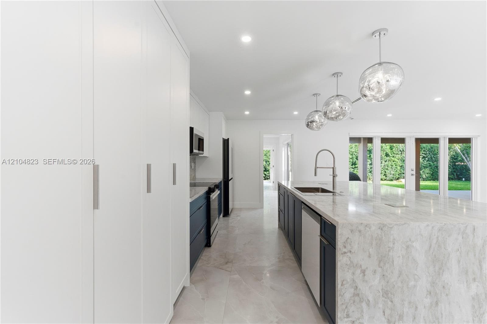 Kitchen featuring floor-to-ceiling cabinetry, a stone-top waterfall island, modern pendant lighting, deep-toned base cabinetry, and large-format tile flooring