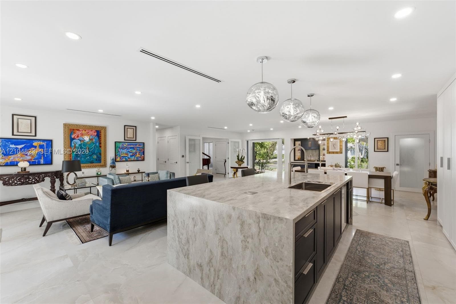 Expansive open-concept living space featuring a large kitchen island with integrated sink, white tile flooring, recessed lighting, and multiple pendant light fixtures