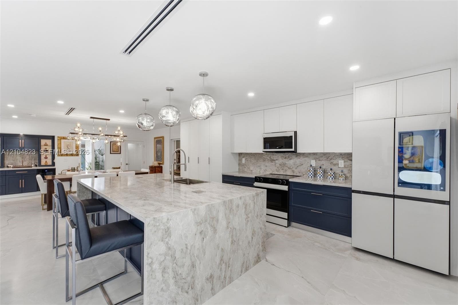 Spacious kitchen featuring a large island with an undermount sink, pendant lighting, two-tone cabinetry, and an integrated refrigerator