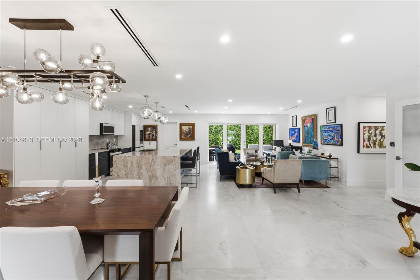 Open-concept living space featuring wood-finish dining table, a large kitchen island with a stone finish, recessed lighting, and expansive glass doors