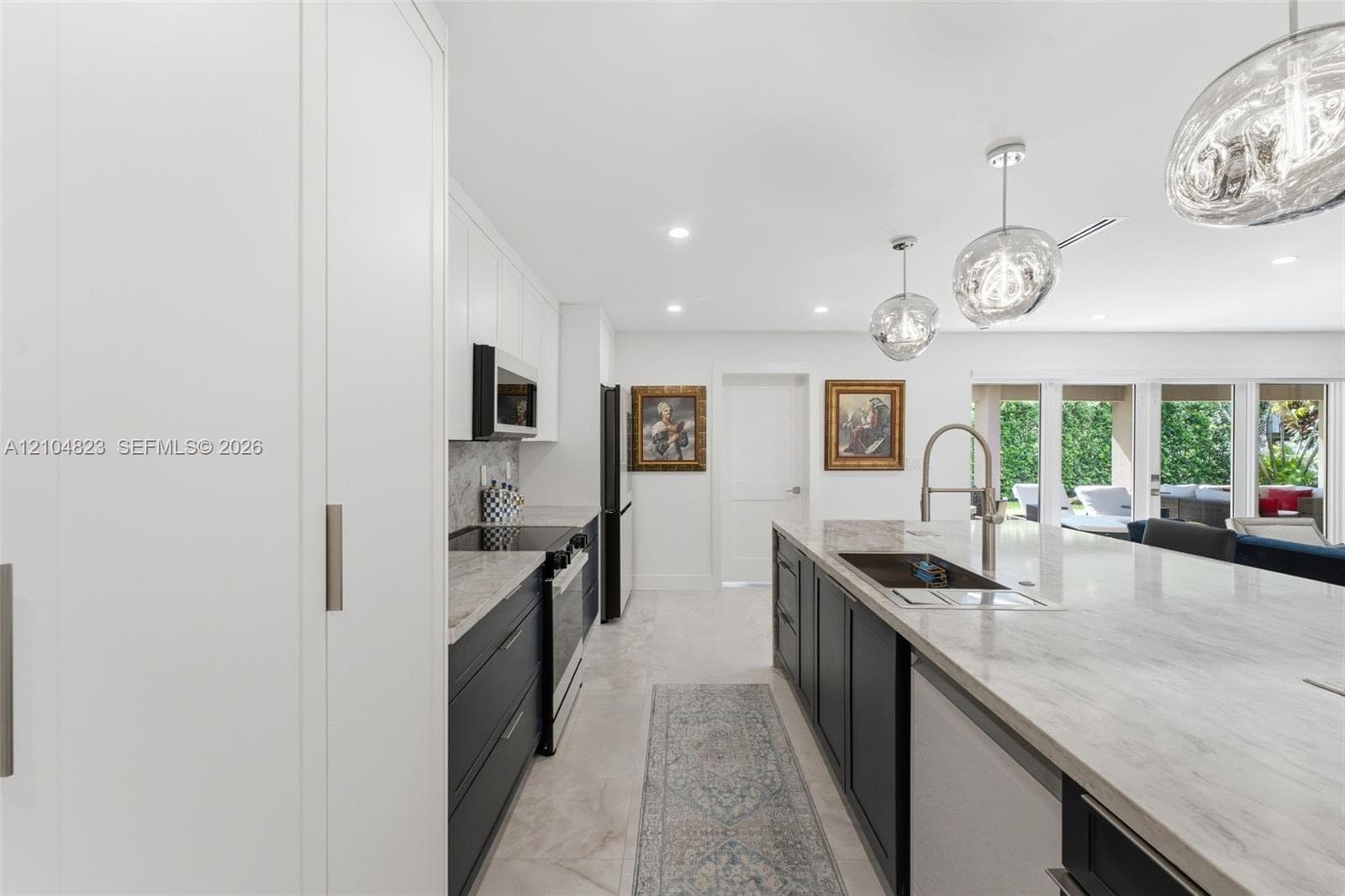 Contemporary kitchen featuring an expansive island with an undermount sink, pendant lighting, built-in appliances, and white flat-panel cabinetry