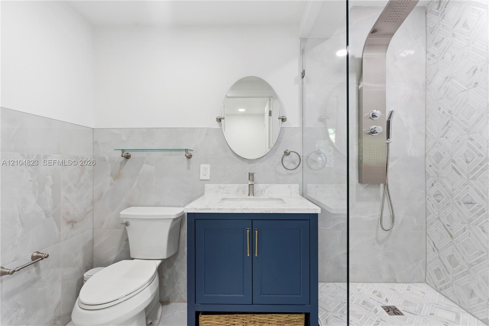 White and grey tiled bathroom featuring a navy vanity with a white countertop, a frameless glass shower enclosure, and a modern shower panel system