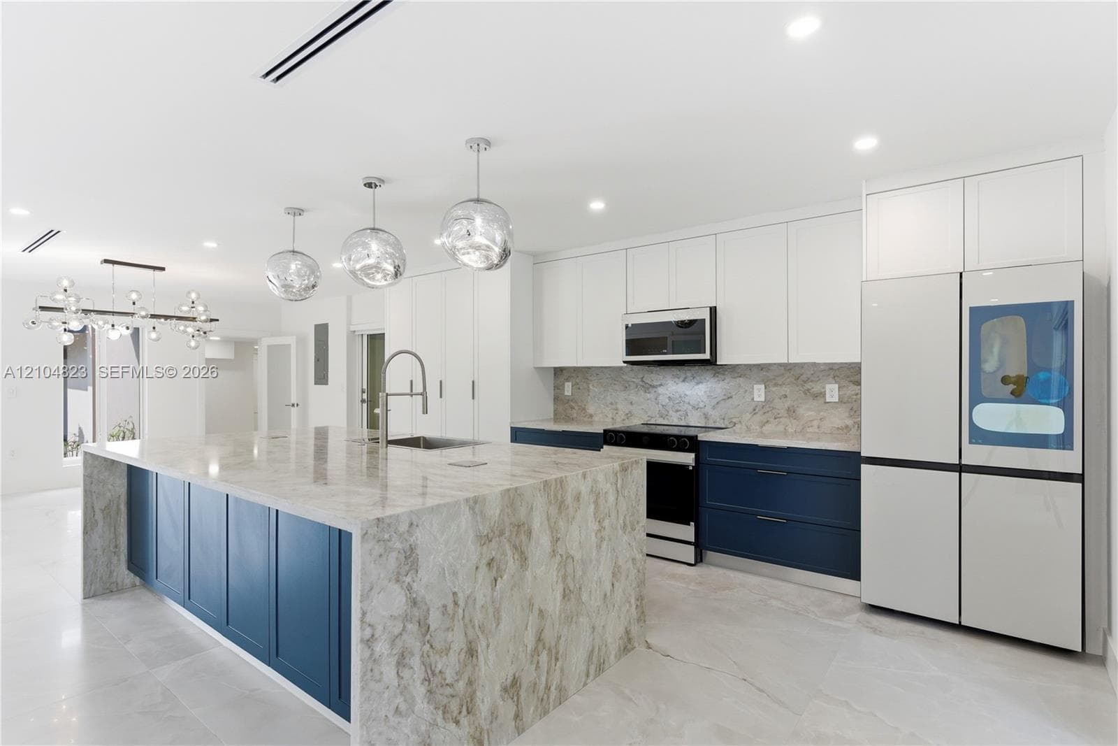Kitchen featuring a large central island with waterfall-edge stone countertops, two-tone cabinetry, stainless steel appliances, and pendant lighting