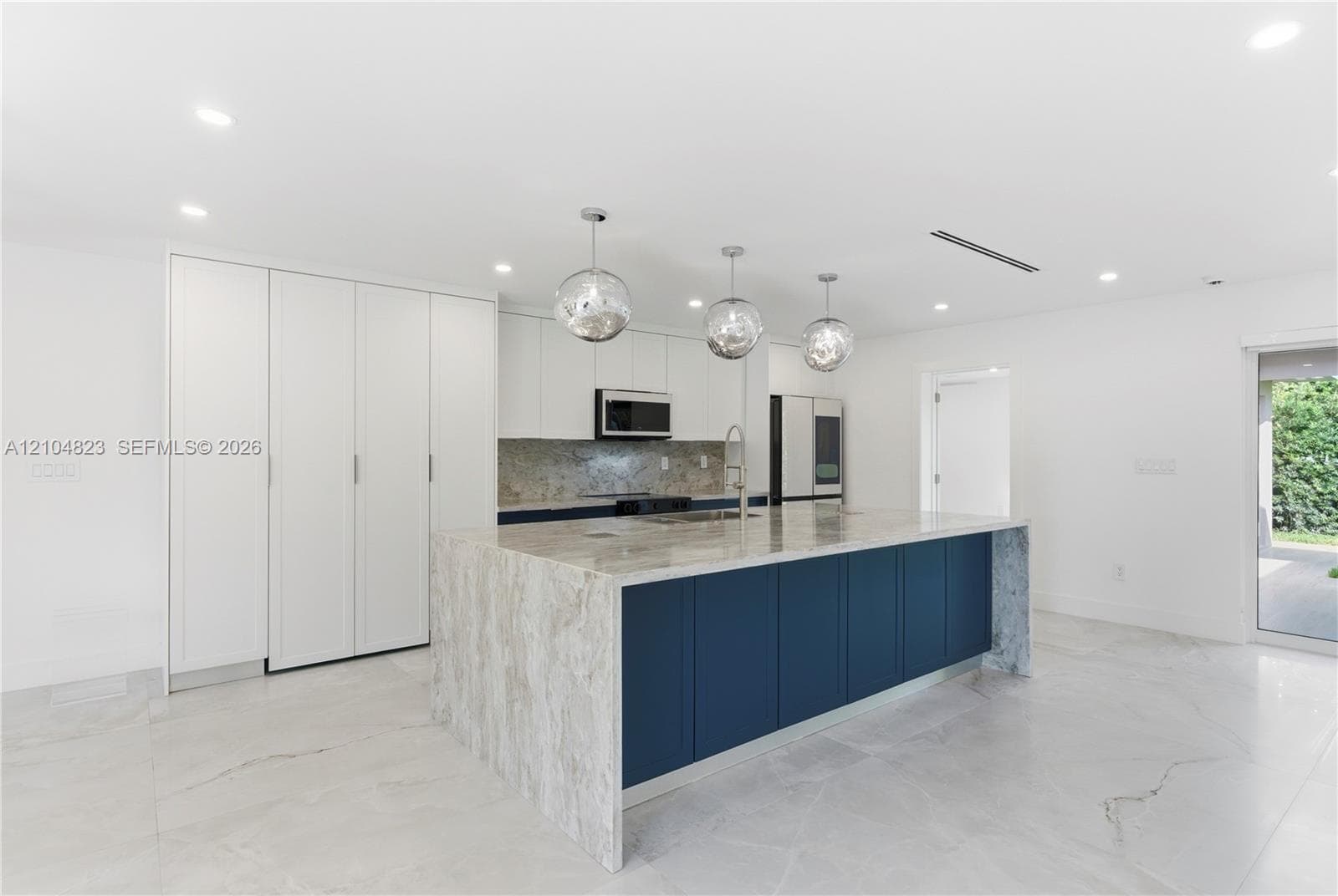 Kitchen featuring floor-to-ceiling cabinetry, a central island with a waterfall countertop, stone backsplash, recessed lighting, and glass pendant fixtures