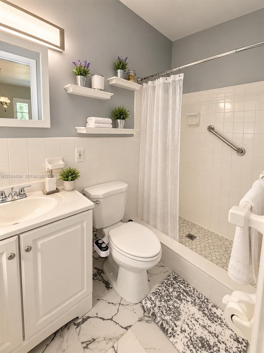 White tile wainscoting and bath surround, white vanity with integrated sink, floating wall shelving, white subway tile shower, and a pebble tile shower floor