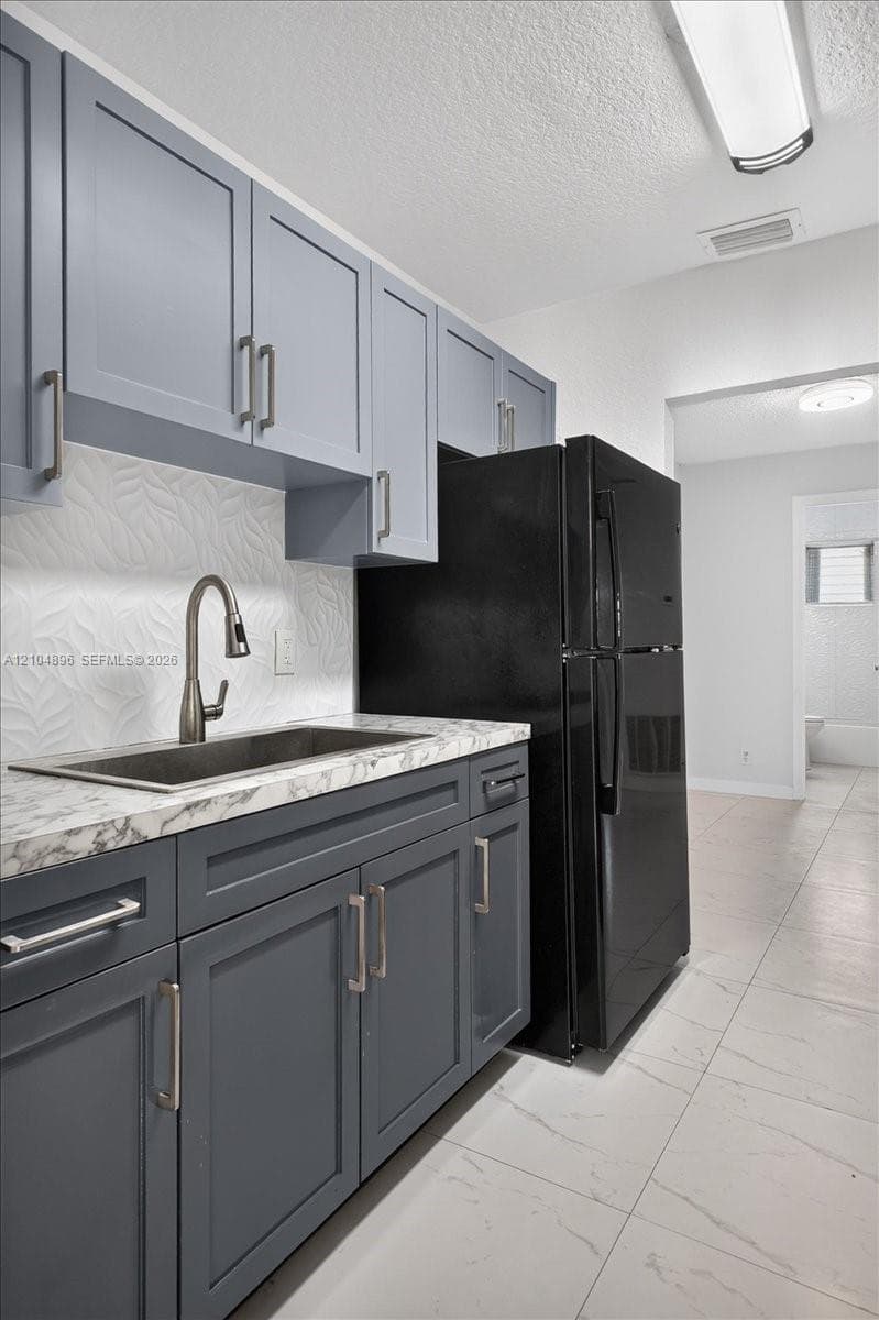 Kitchen featuring two-tone shaker-style cabinetry, stone-patterned countertops, a textured tile backsplash, an undermount sink with a gooseneck faucet, and large-format tile flooring