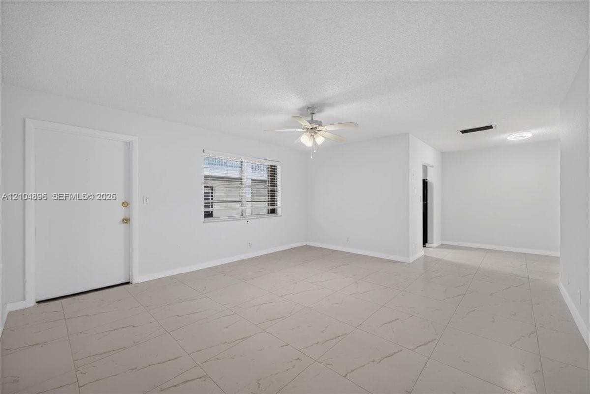 Interior space featuring light-toned tile flooring, neutral walls, a multi-blade ceiling fan with integrated lighting, and a window with horizontal blinds