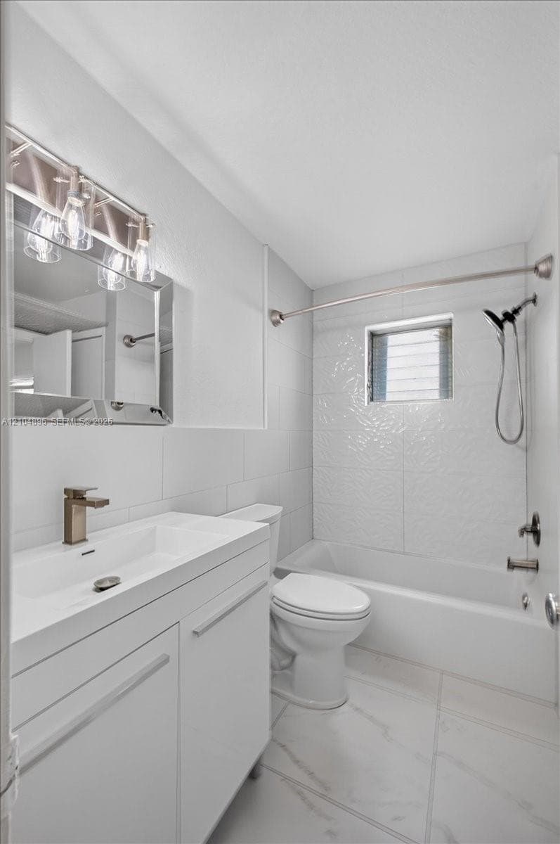 Bathroom featuring a white vanity with a rectangular sink, metallic faucet, wall-mounted mirror with integrated light fixture, and a white tile bathtub surround