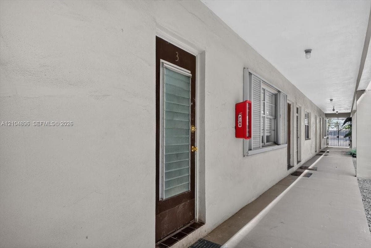 Exterior corridor featuring smooth-finish stucco walls, metal-frame doors with louvered glass inserts, and recessed ceiling lighting