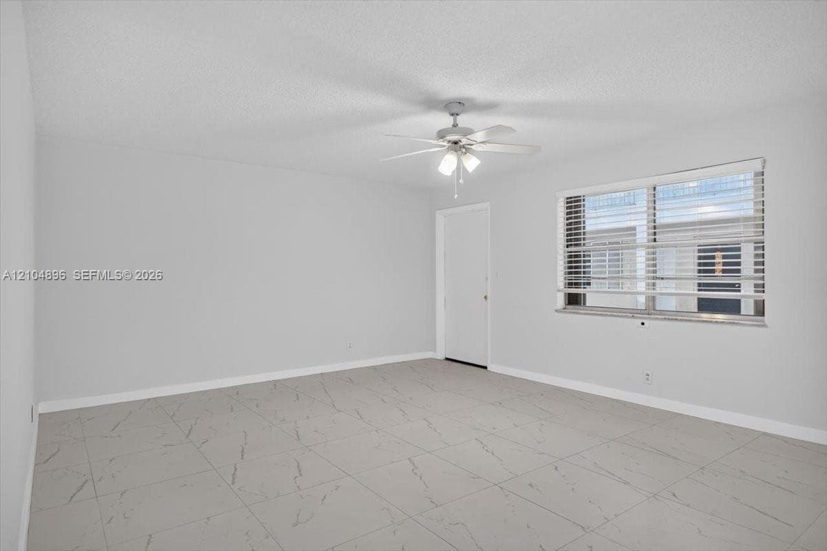 Interior space featuring large-format tile flooring with a neutral vein pattern, a ceiling fan with integrated light fixture, and a window with horizontal blinds
