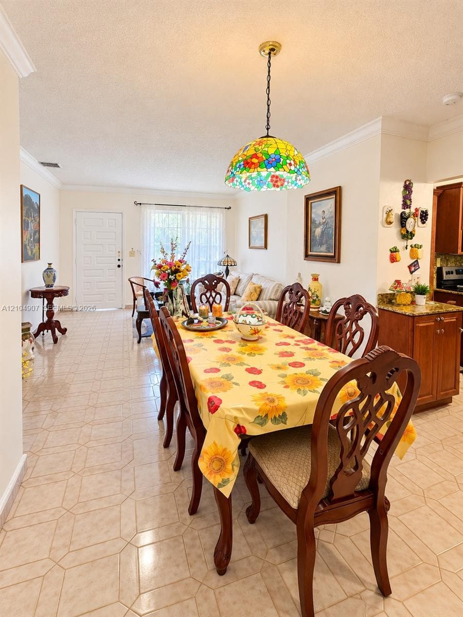 Open-concept interior featuring geometric tile flooring, crown molding, a decorative stained-glass pendant light fixture, and wood-finish cabinetry with stone-look countertops