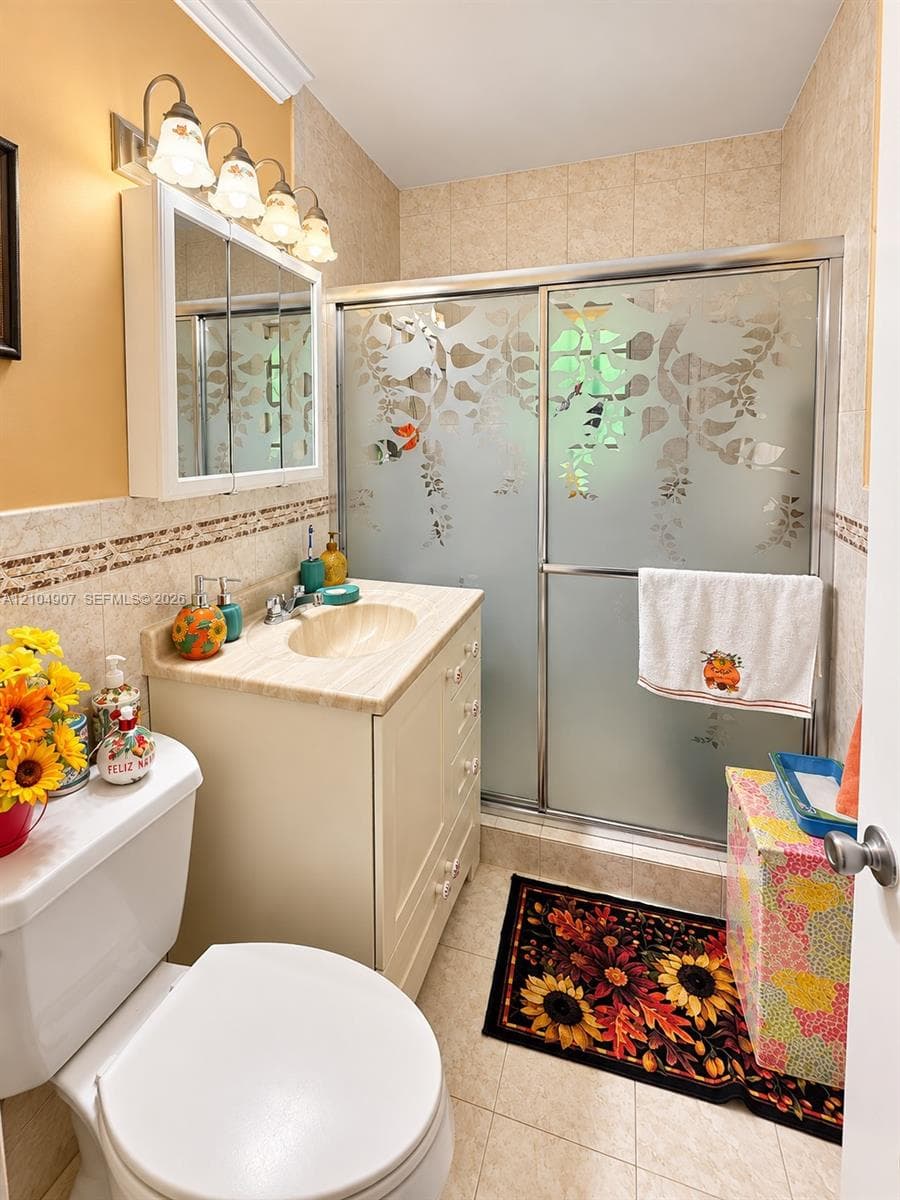 Bathroom featuring a vanity with integrated sink, etched glass sliding shower doors, decorative tiled wall accents, and a mirrored medicine cabinet with four-light fixture
