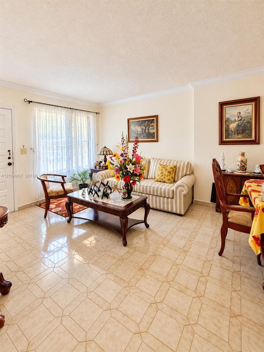 Living space featuring large-format ceramic tile flooring, crown molding, and an expansive window with hardware-mounted drapery