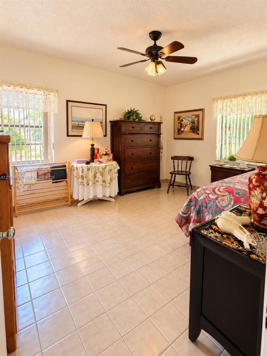 Spacious room featuring neutral ceramic tile flooring, two windows with vertical blinds, and a multi-blade ceiling fan with integrated lighting