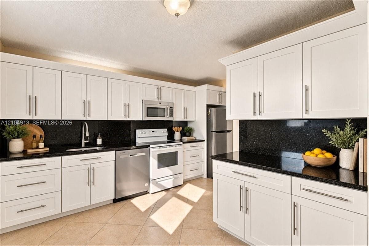 Kitchen featuring white shaker-style cabinetry, dark stone countertops, tile flooring, and stainless steel appliances