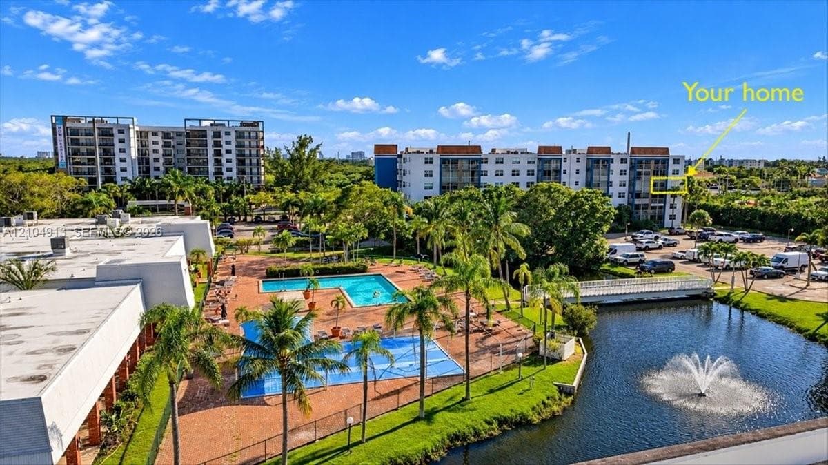 Aerial perspective of a multi-story residential building complex featuring an outdoor swimming pool, paved pool deck, water feature with fountain, and mature palm trees