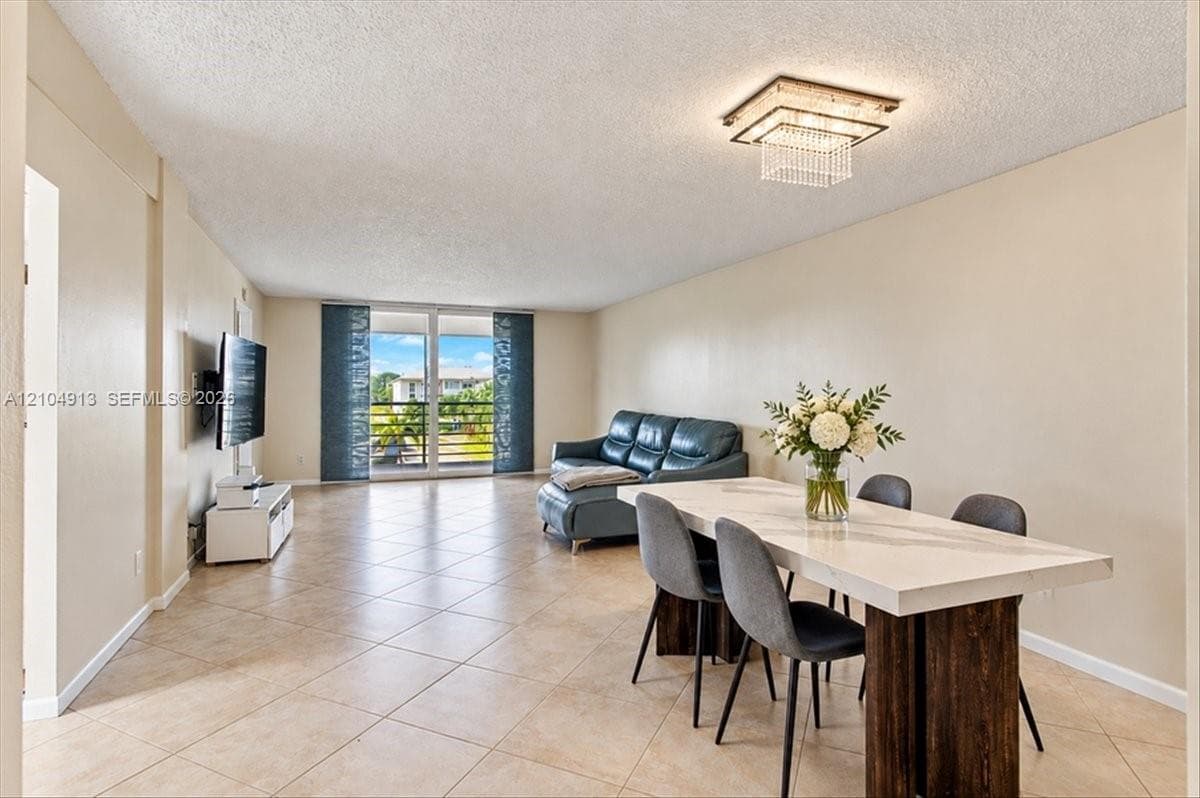 Neutral-toned ceramic tile flooring, tiered crystal flush-mount light fixture, and floor-to-ceiling glass sliding doors leading to an exterior balcony