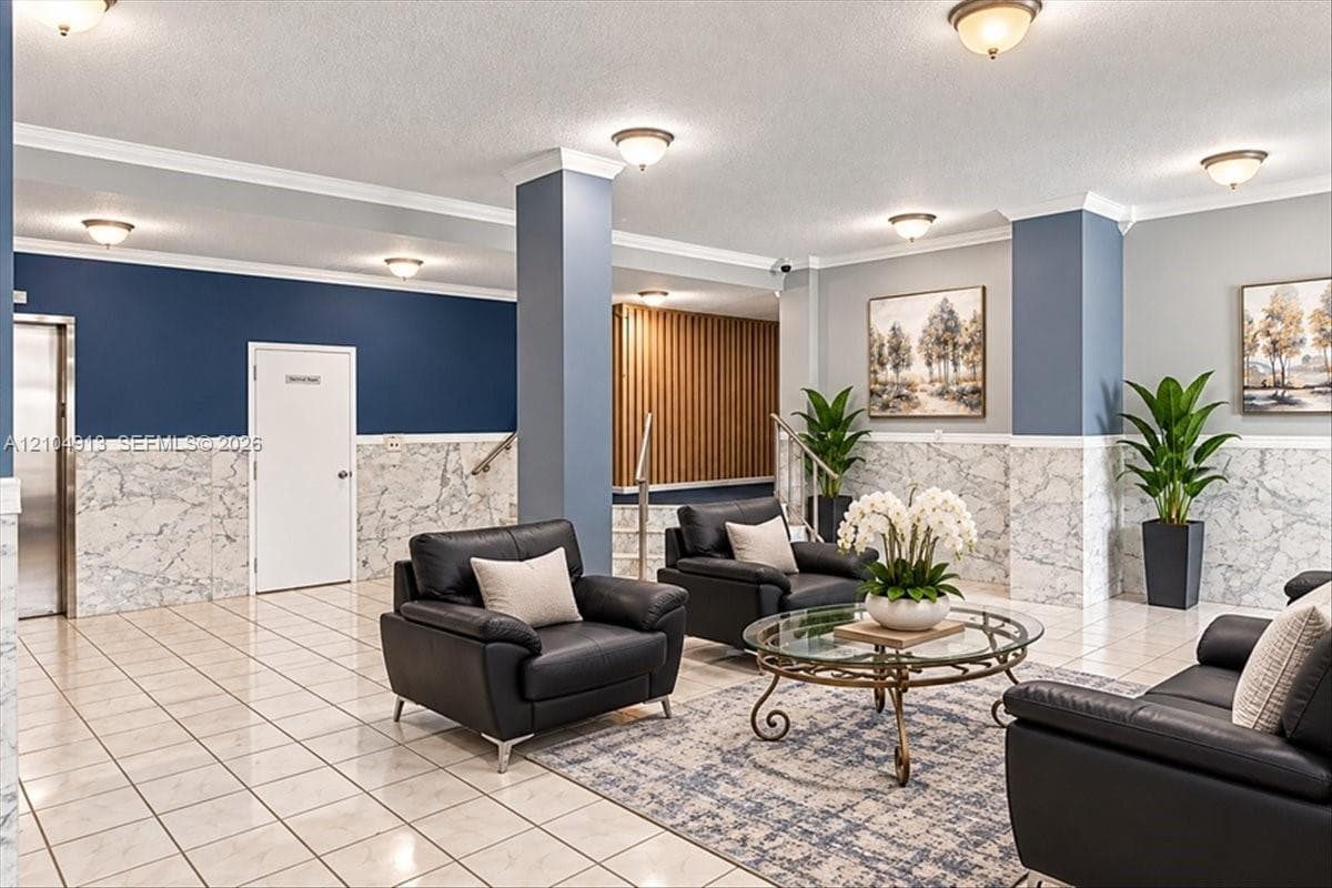 Building lobby featuring polished tile flooring, stone-patterned wainscoting, crown molding, built-in structural columns, and recessed lighting