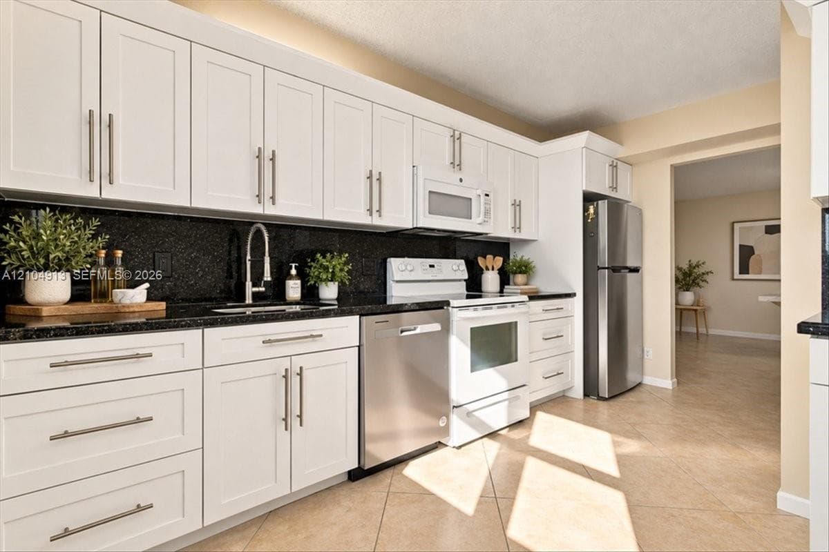 Kitchen featuring white shaker-style cabinetry, dark stone countertops, stainless steel appliances, and tile flooring