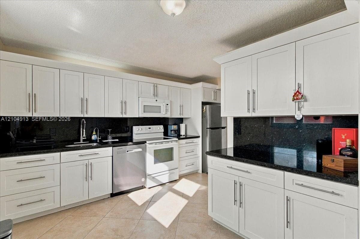 Kitchen featuring white shaker-style cabinetry, dark stone countertops, tile flooring, and stainless steel appliances