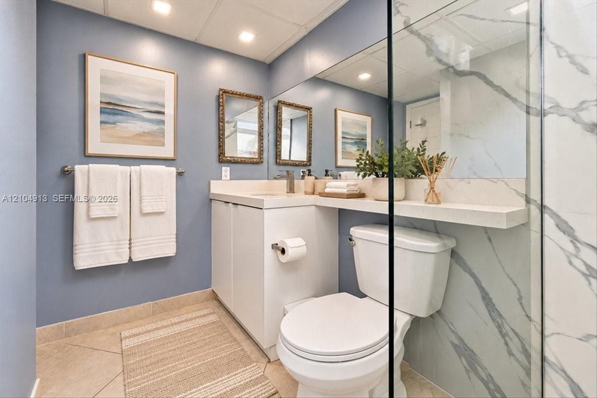 Bathroom featuring a vanity with integrated countertop and shelf, full-width wall mirror, recessed lighting, and shower enclosure with large-format stone-pattern tile surrounds