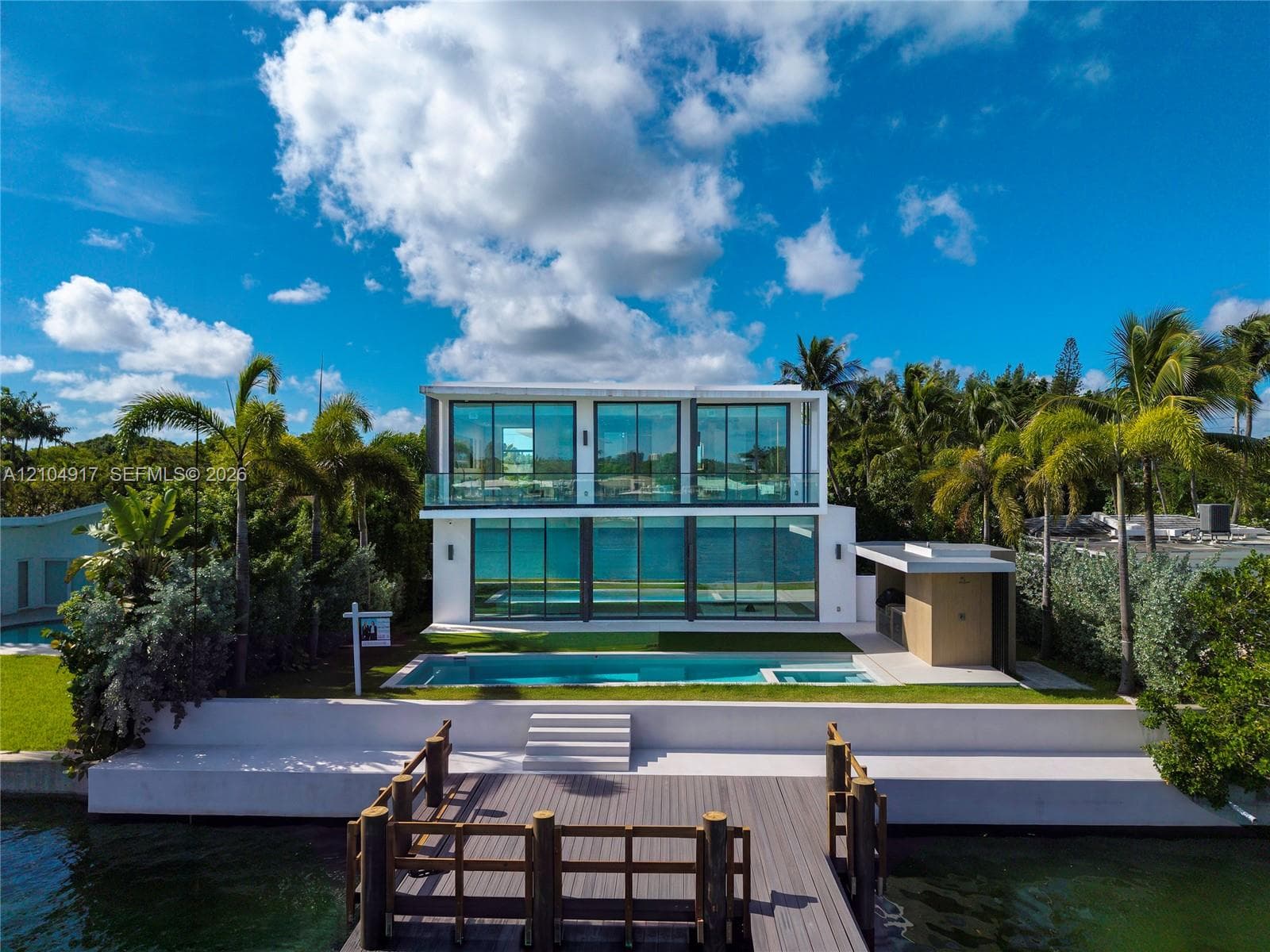 Modern two-story waterfront residence featuring floor-to-ceiling glass walls, a private swimming pool with integrated spa, and a wooden boat dock