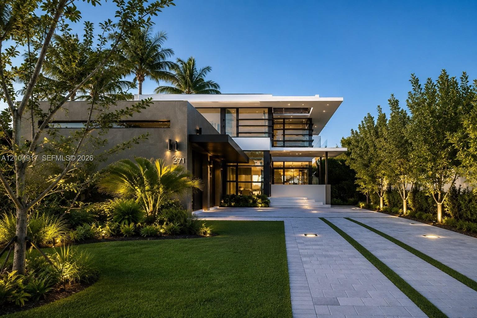 Modern two-story architectural exterior featuring smooth stucco finish, expansive glass windows, integrated landscape lighting, and a paved driveway with linear grass accents